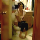A girl is seen through an open bathroom door taking a shit on the toilet.